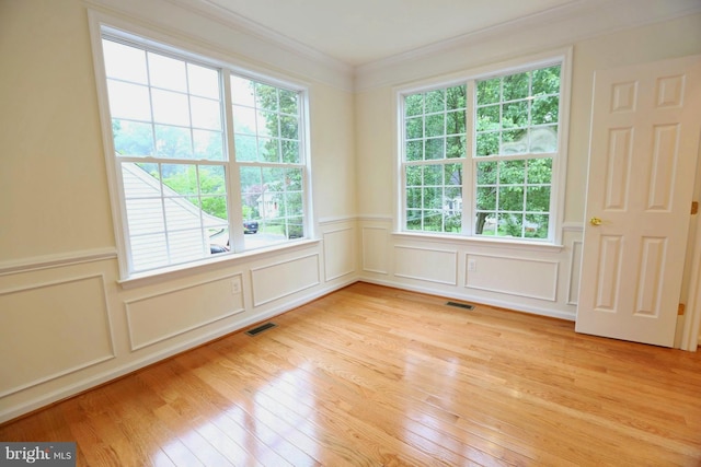 spare room with plenty of natural light, visible vents, light wood-style flooring, and ornamental molding