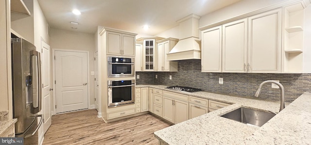 kitchen featuring custom exhaust hood, backsplash, appliances with stainless steel finishes, a sink, and light stone countertops