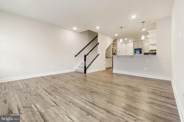 unfurnished living room with light wood-style floors, recessed lighting, stairway, and baseboards