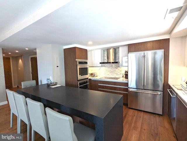 kitchen with visible vents, a breakfast bar, wood finished floors, stainless steel appliances, and wall chimney range hood