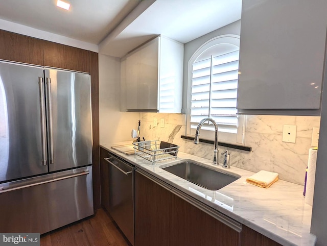 kitchen with dark wood-style flooring, a sink, appliances with stainless steel finishes, light stone countertops, and tasteful backsplash