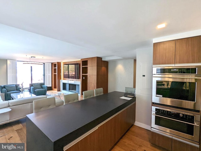 kitchen featuring a peninsula, dark countertops, stainless steel double oven, and wood finished floors