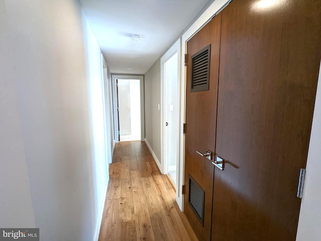 hall featuring light wood-style floors, baseboards, and visible vents