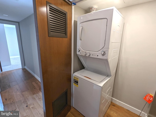 clothes washing area featuring stacked washer and clothes dryer, visible vents, light wood-style flooring, laundry area, and baseboards