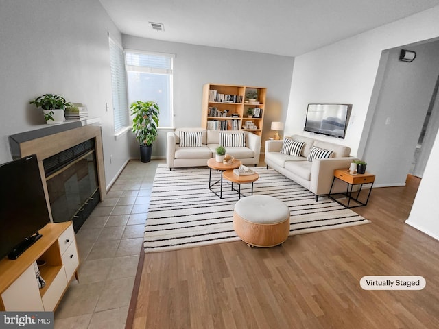 living area featuring wood finished floors, a glass covered fireplace, visible vents, and baseboards