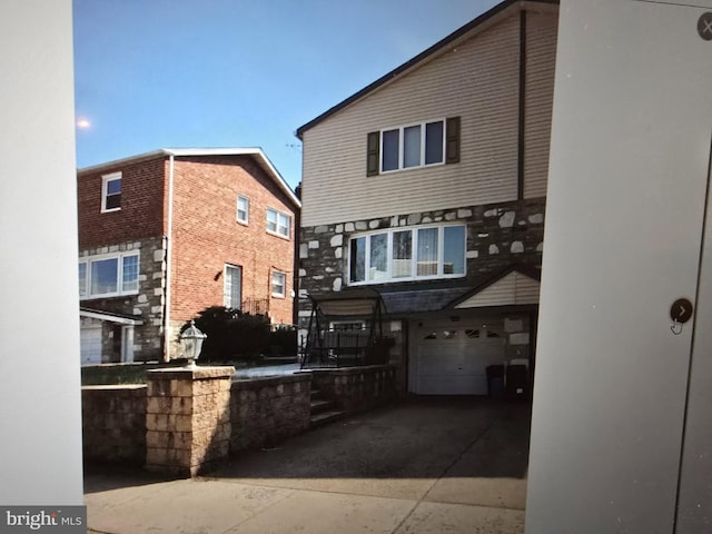 back of property with stone siding, an attached garage, and driveway