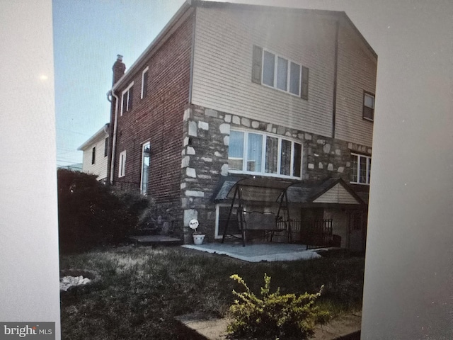 back of house featuring stone siding, a patio area, and a chimney