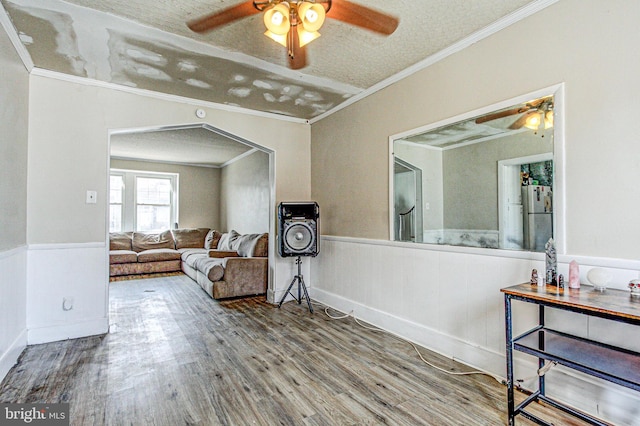 living room featuring a wainscoted wall, arched walkways, wood finished floors, and crown molding