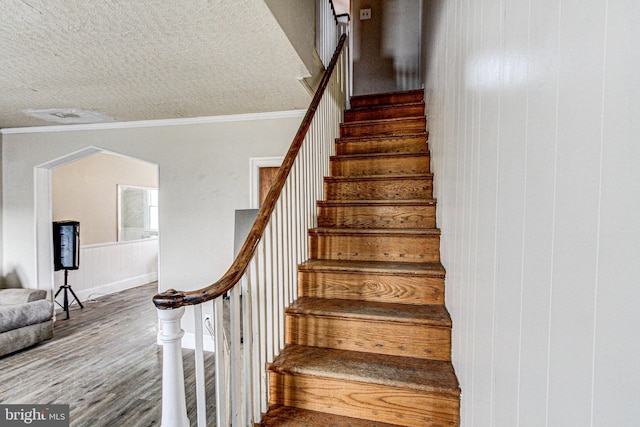 stairway with a textured ceiling, ornamental molding, and wood finished floors