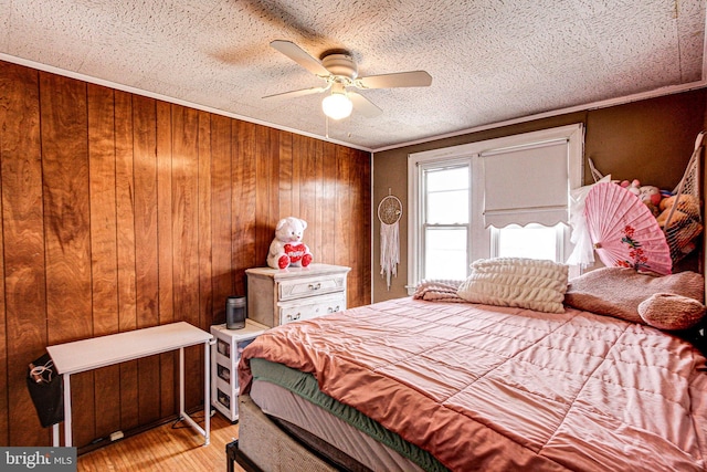 bedroom featuring wooden walls, a ceiling fan, light wood-style flooring, crown molding, and a textured ceiling