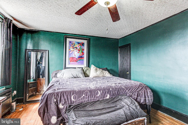 bedroom with ceiling fan, a textured ceiling, baseboards, and wood finished floors