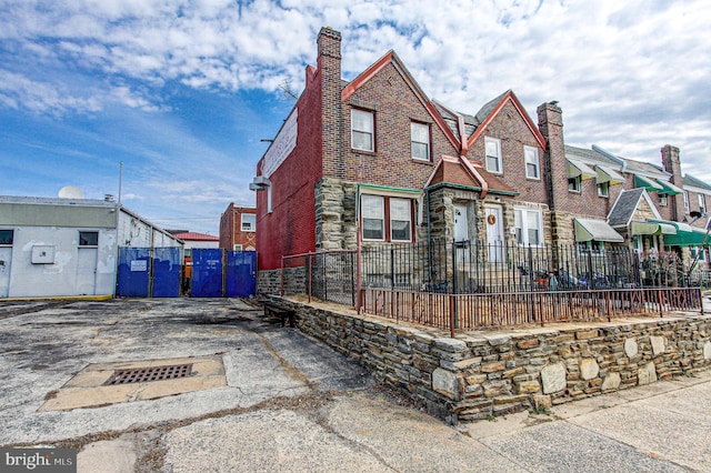 view of front of house with stone siding, a chimney, fence, and brick siding