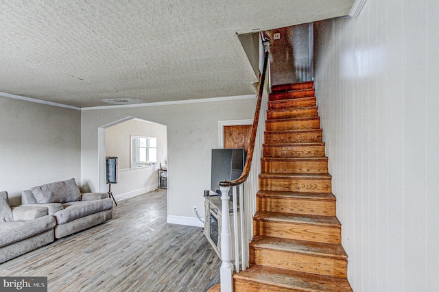 stairway featuring arched walkways, ornamental molding, wood finished floors, and baseboards