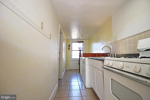 kitchen featuring light tile patterned floors, white gas range oven, decorative backsplash, white cabinetry, and a sink