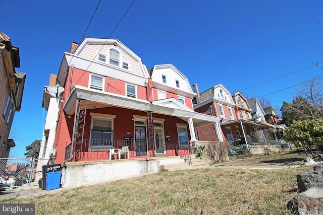 view of front of property with a porch, a chimney, a front yard, and a gambrel roof