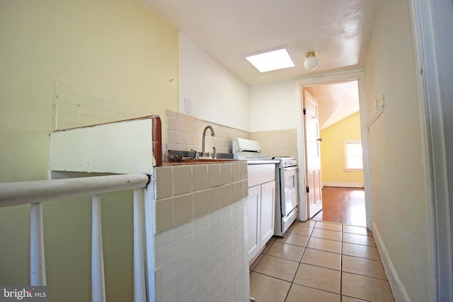 interior space featuring light tile patterned floors, a skylight, decorative backsplash, gas range gas stove, and a sink