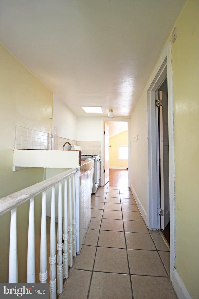 hallway with light tile patterned floors, baseboards, and lofted ceiling with skylight