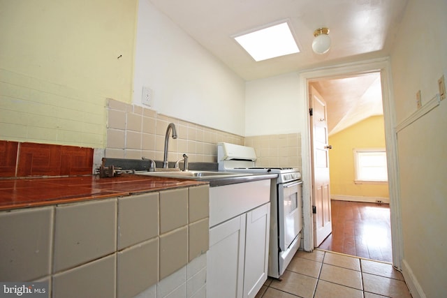 kitchen featuring light tile patterned flooring, a sink, white gas range, tasteful backsplash, and dark countertops