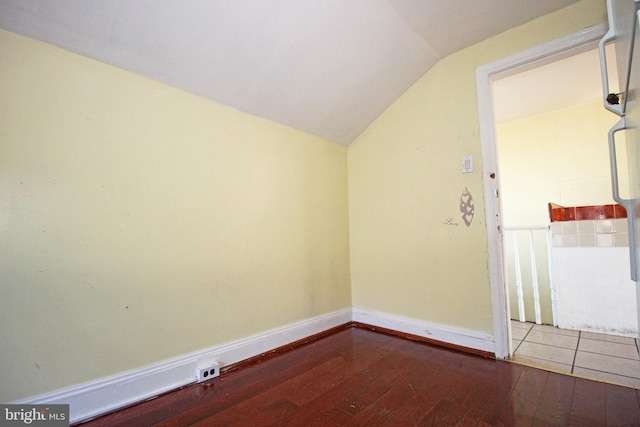 empty room featuring lofted ceiling, wood-type flooring, and baseboards