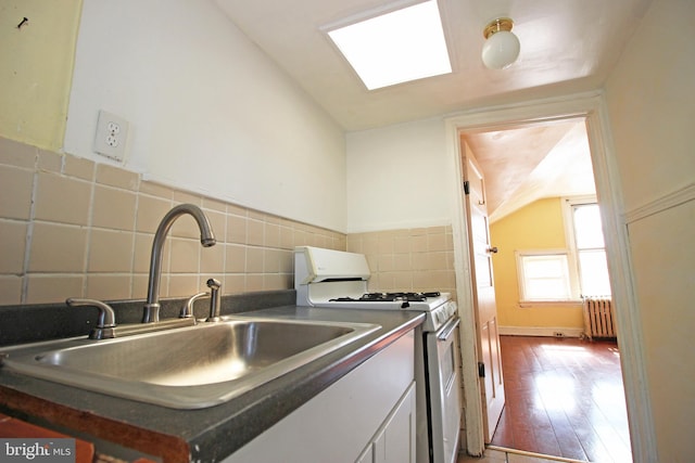 kitchen featuring white gas stove, wood finished floors, a sink, radiator, and dark countertops