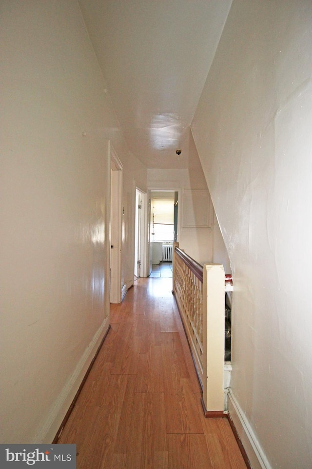 hallway featuring radiator heating unit, baseboards, and light wood-style flooring