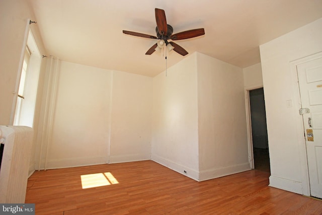 spare room featuring ceiling fan, radiator, wood finished floors, and baseboards