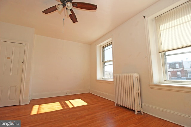 unfurnished room featuring radiator heating unit, wood finished floors, a ceiling fan, and baseboards