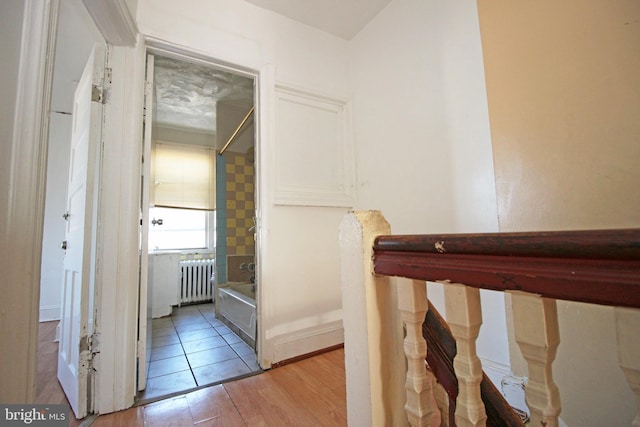 hall featuring light wood-style floors, radiator heating unit, baseboards, and an upstairs landing