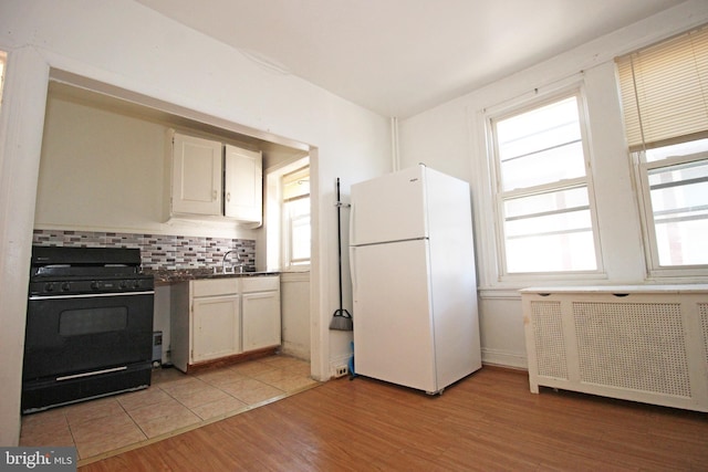 kitchen featuring light wood-type flooring, black range with gas stovetop, freestanding refrigerator, decorative backsplash, and radiator