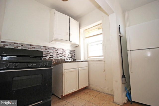 kitchen featuring backsplash, black gas range oven, freestanding refrigerator, light tile patterned flooring, and a sink