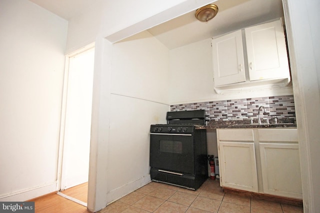 kitchen featuring tasteful backsplash, dark countertops, white cabinetry, a sink, and gas stove