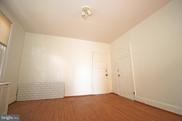 unfurnished room featuring radiator heating unit, baseboards, and wood finished floors