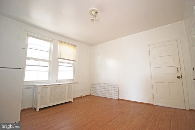 spare room with baseboards, light wood-style flooring, and radiator