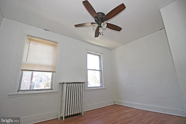 empty room featuring radiator heating unit, baseboards, ceiling fan, and wood finished floors