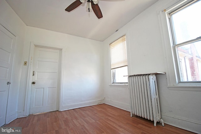 empty room featuring radiator, ceiling fan, baseboards, and wood finished floors