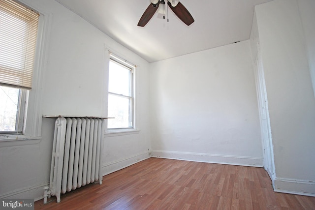 spare room featuring baseboards, ceiling fan, radiator heating unit, and wood finished floors