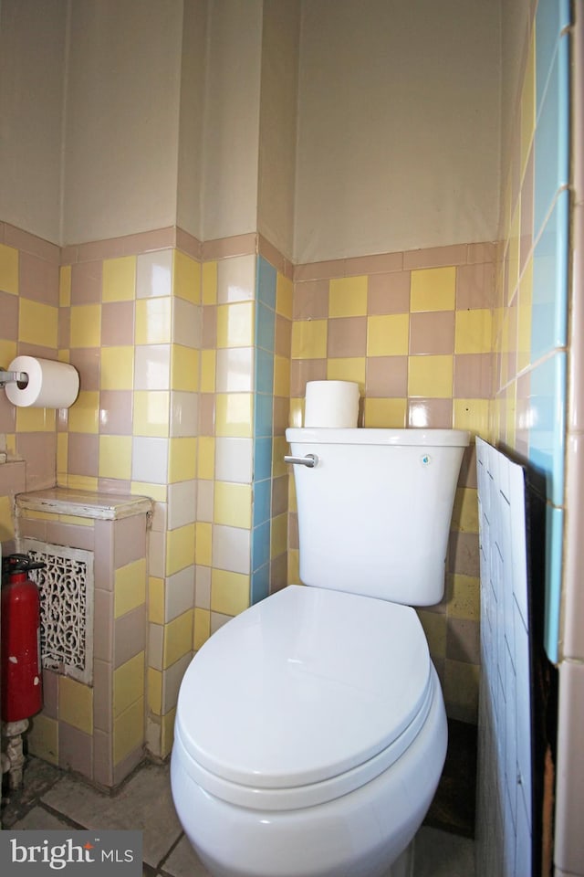 half bath with toilet, tile patterned flooring, and tile walls