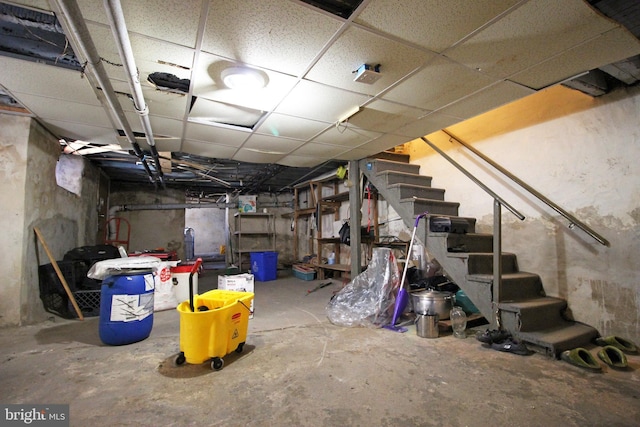 basement featuring a paneled ceiling and stairs