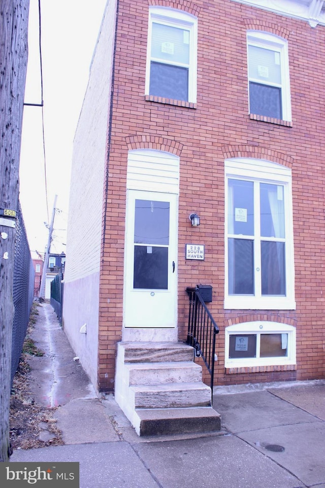 townhome / multi-family property with entry steps, brick siding, and fence