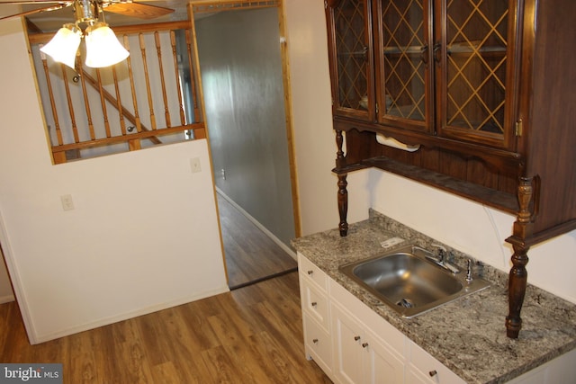 kitchen featuring baseboards, ceiling fan, wood finished floors, white cabinetry, and a sink