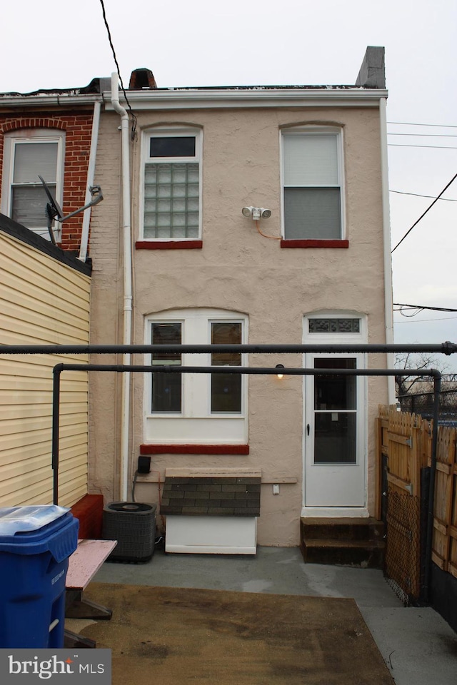 view of front of house with entry steps, central AC unit, fence, and stucco siding