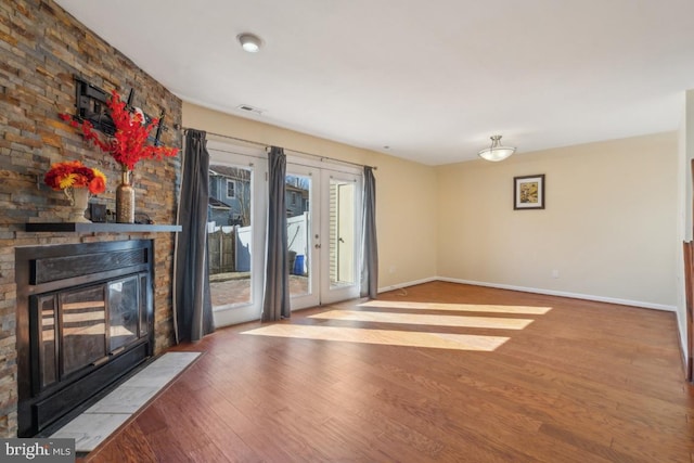 unfurnished living room with french doors, visible vents, a stone fireplace, wood finished floors, and baseboards