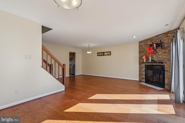 unfurnished living room with stairs, a stone fireplace, wood finished floors, and baseboards