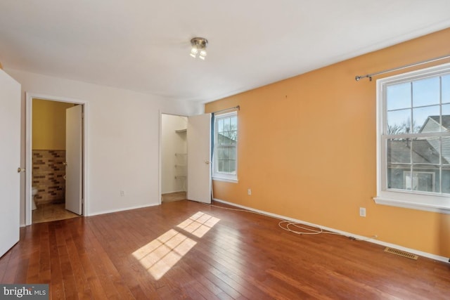 unfurnished bedroom with baseboards, visible vents, wood-type flooring, a spacious closet, and a closet