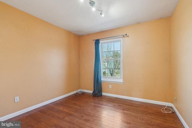 spare room featuring wood finished floors, visible vents, and baseboards