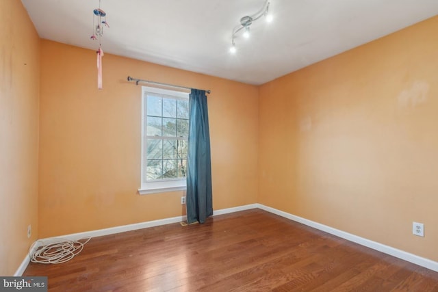 unfurnished room featuring rail lighting, baseboards, and wood finished floors