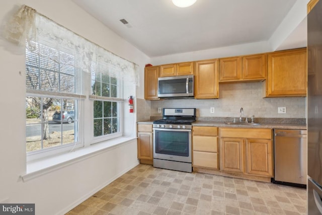 kitchen with light floors, appliances with stainless steel finishes, a sink, and tasteful backsplash