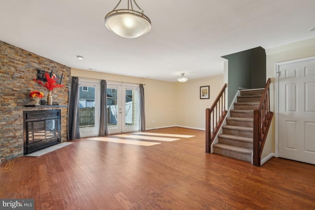 unfurnished living room with a stone fireplace, wood finished floors, baseboards, stairs, and french doors