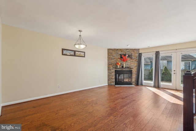 unfurnished living room with baseboards, french doors, wood finished floors, and a stone fireplace