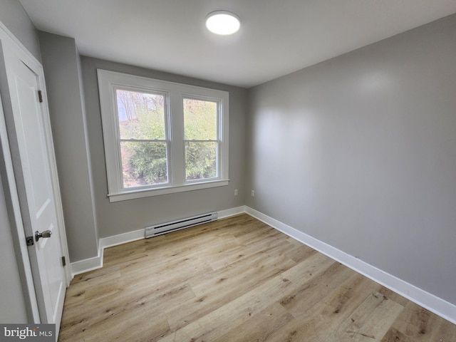 empty room featuring light wood-type flooring, a baseboard radiator, and baseboards